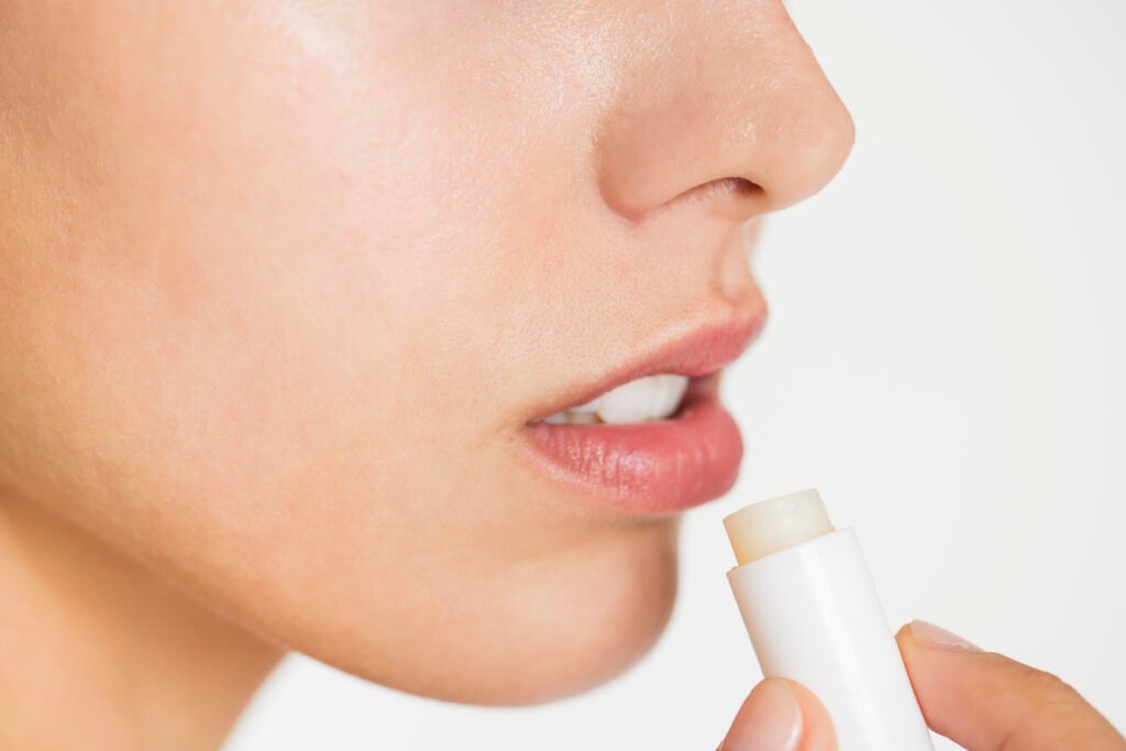 Mulher aplicando hidratante Labial. Ao escolher fórmulas com ativos como manteiga de karité, vitamina E ou ácido hialurônico, que promovem reparação e nutrição profunda, você deixa seus lábios sempre suaves e saudáveis.