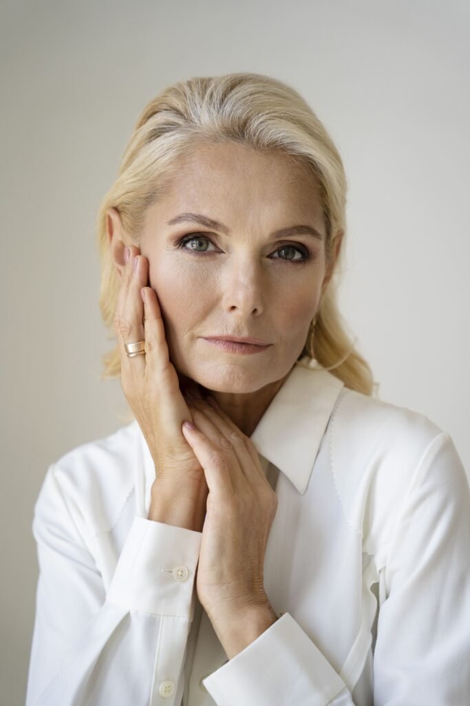 Imagem de uma mulher de 50 anos exibindo seu rosto com linhas finas, rugas e sinais de perda de firmeza na pele. A fotografia destaca a textura natural da pele madura, evidenciando os efeitos do envelhecimento cutâneo.